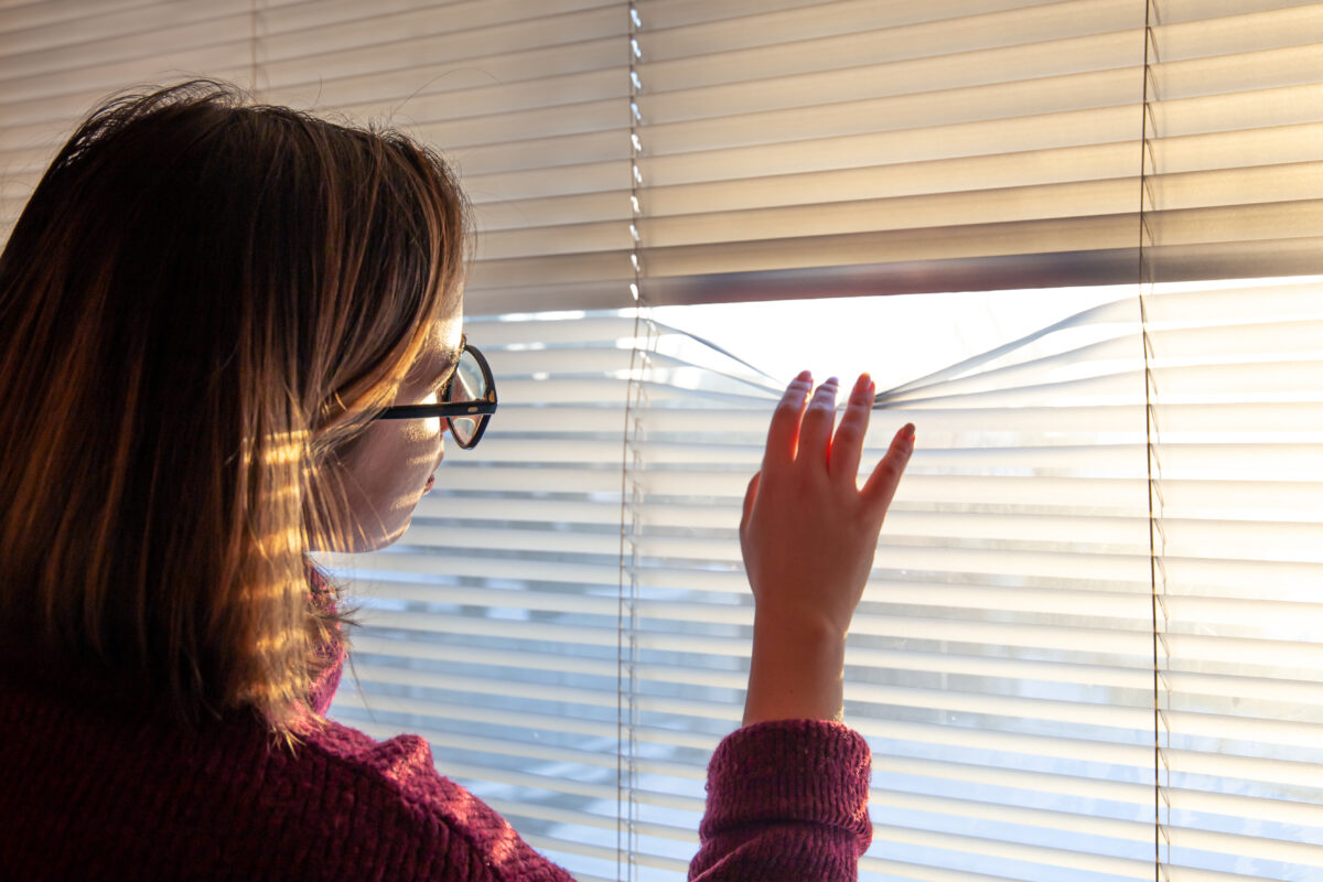 woman looks through blinds early morning sunlight